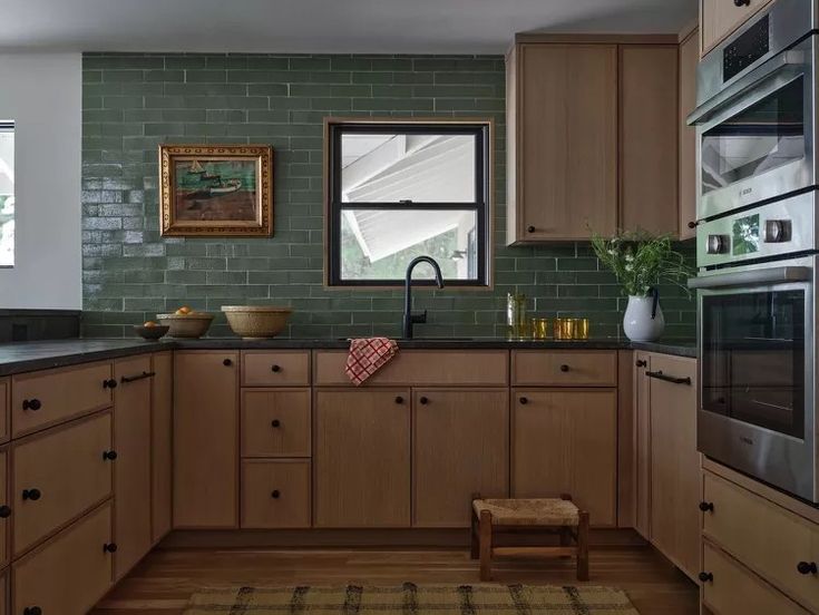 a kitchen with green brick walls and wooden cabinets, an oven, sink, dishwasher, microwave and stool