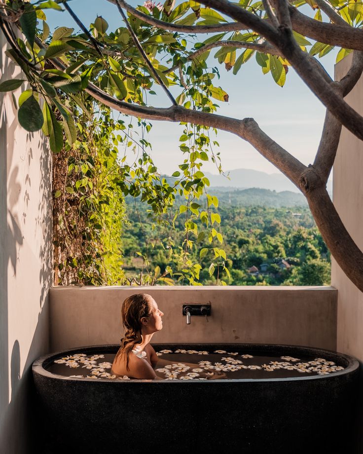 a woman sitting in an outdoor jacuzzi tub overlooking the trees and hills below