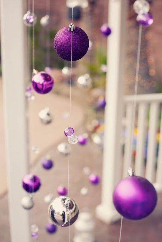 purple and silver ornaments are hanging from the ceiling in front of a white porch railing