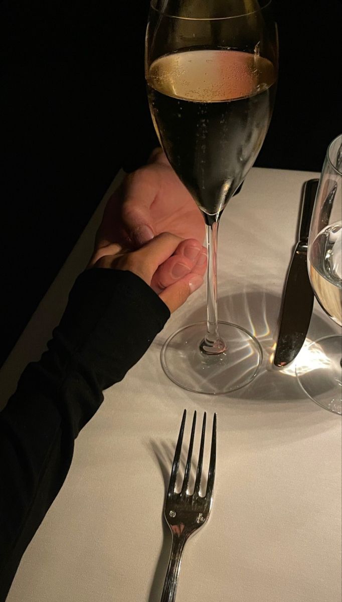 two people holding hands at a table with wine and silverware in front of them