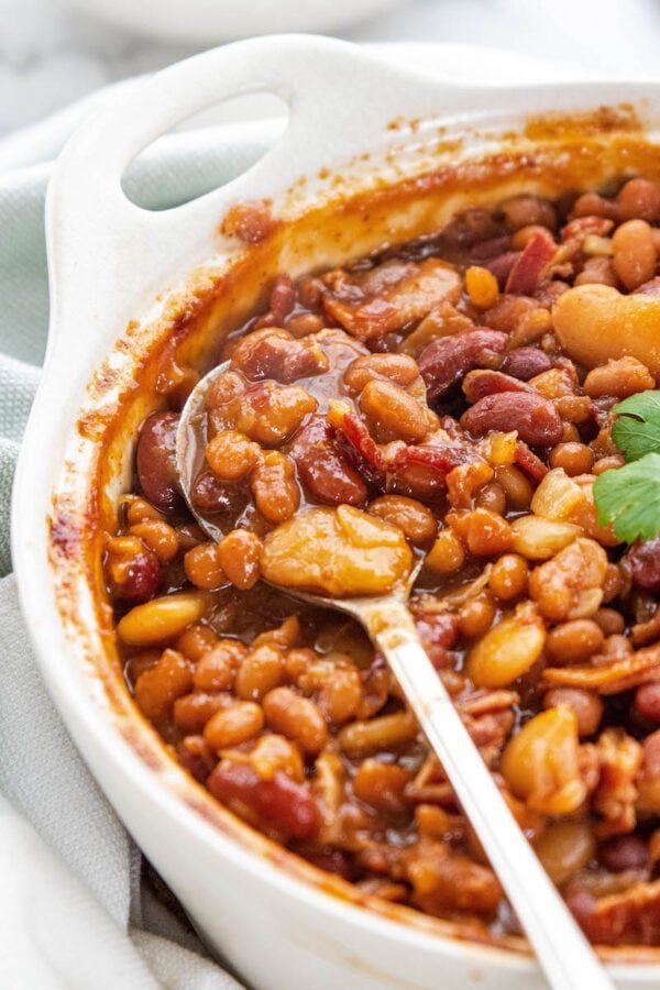 a white bowl filled with beans and meat on top of a table next to a spoon