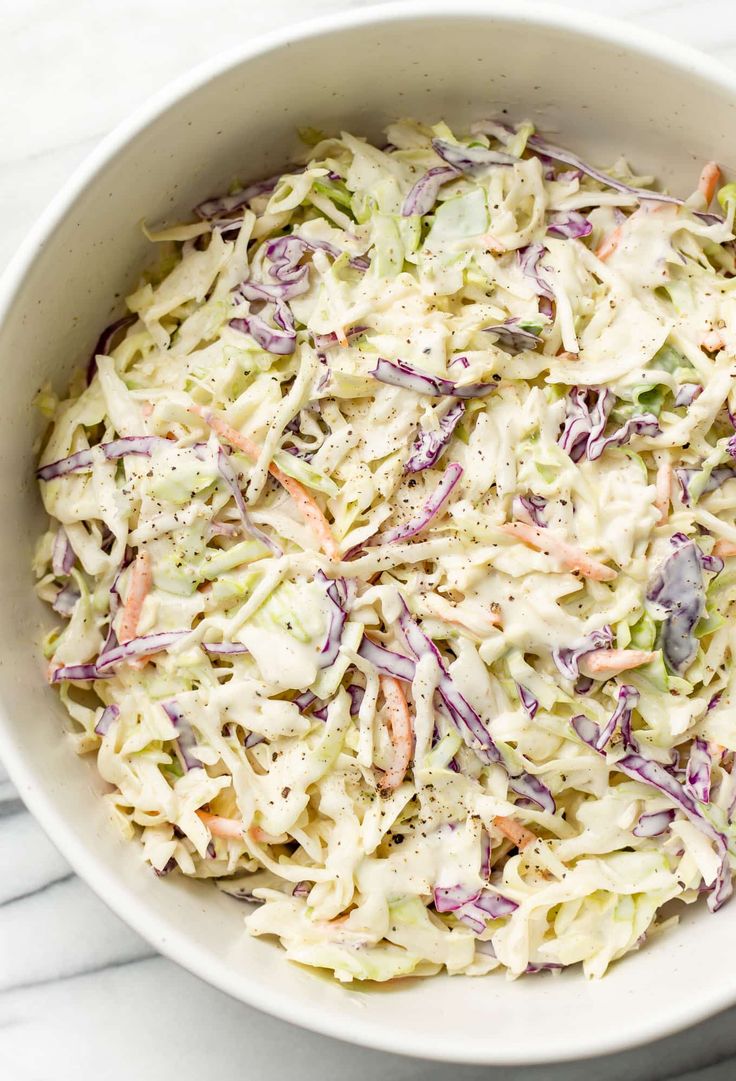 a white bowl filled with coleslaw salad on top of a marble countertop