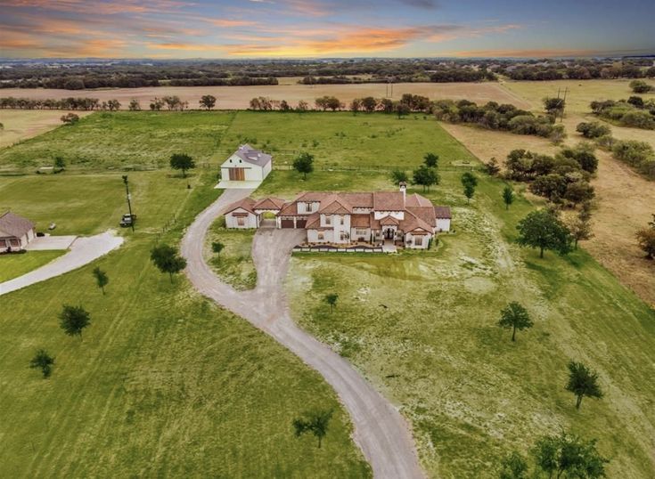 an aerial view of a large home in the middle of a field with trees and grass