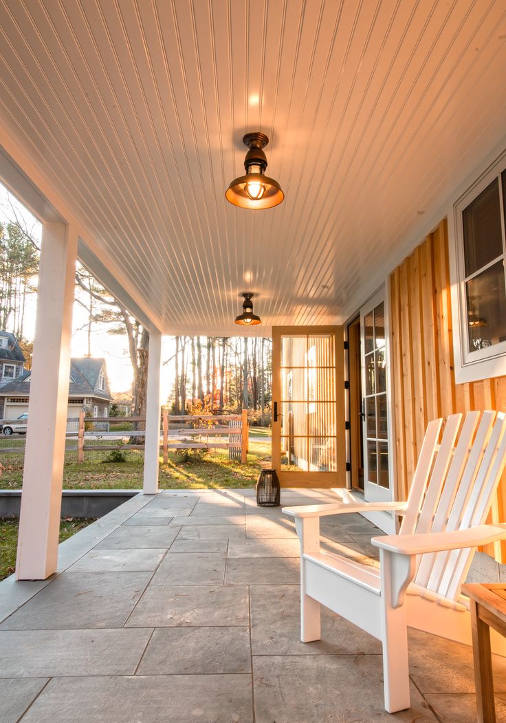 a white chair sitting on top of a porch next to a light fixture and windows