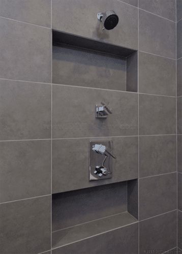 the shower head is mounted to the wall in this bathroom with gray tile and stainless steel fixtures