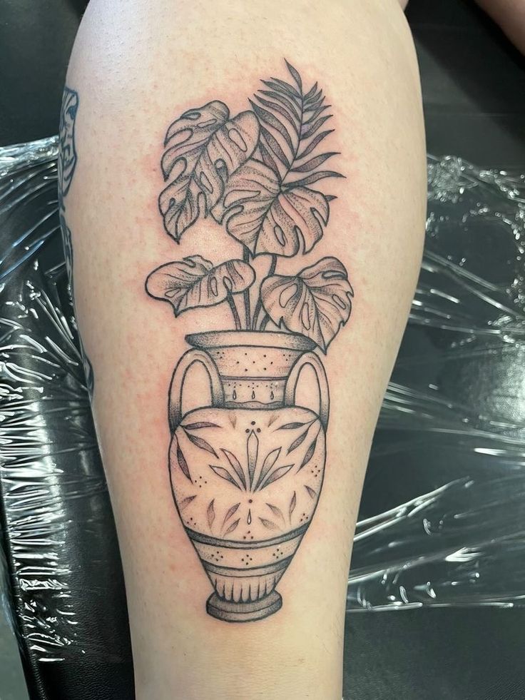 a black and white photo of a potted plant with leaves on the side of a woman's leg