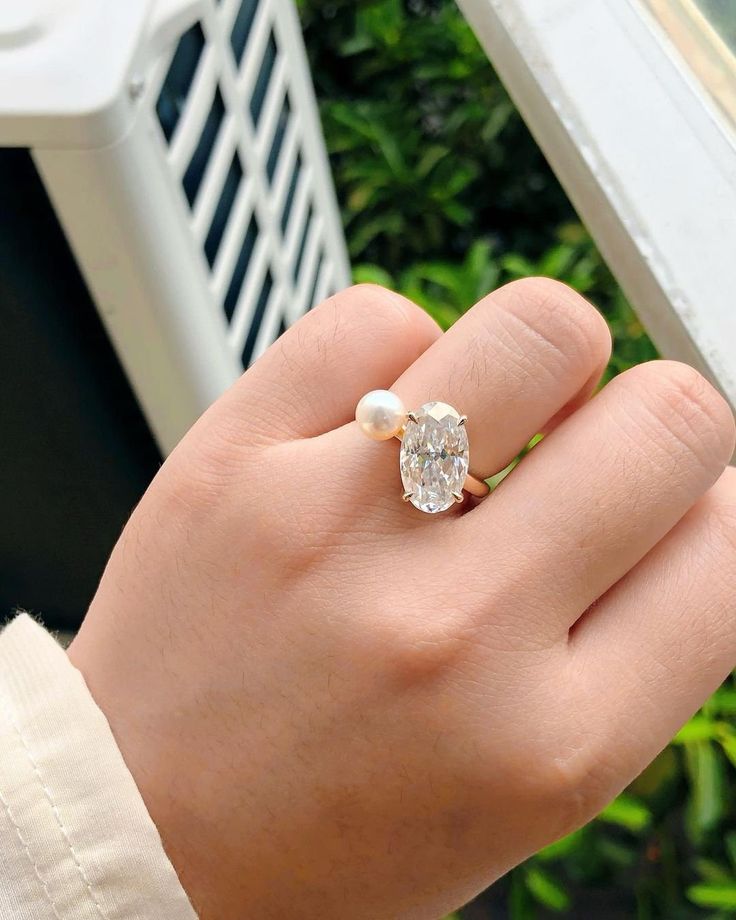 a woman's hand holding a ring with a diamond and pearl in the middle