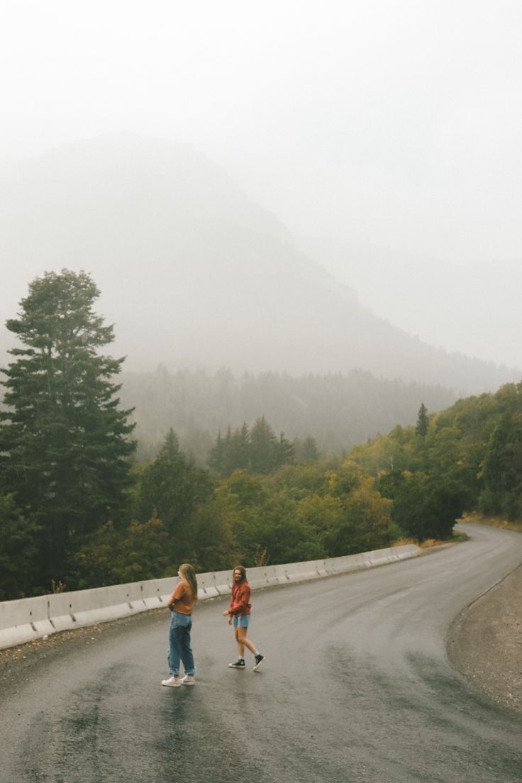 two people walking down the road on a foggy day with mountains in the background