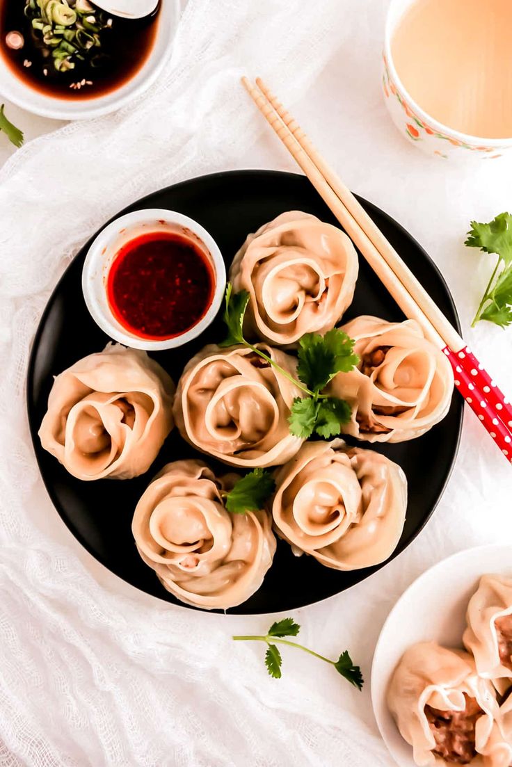 some dumplings on a plate with dipping sauce and chopsticks next to them