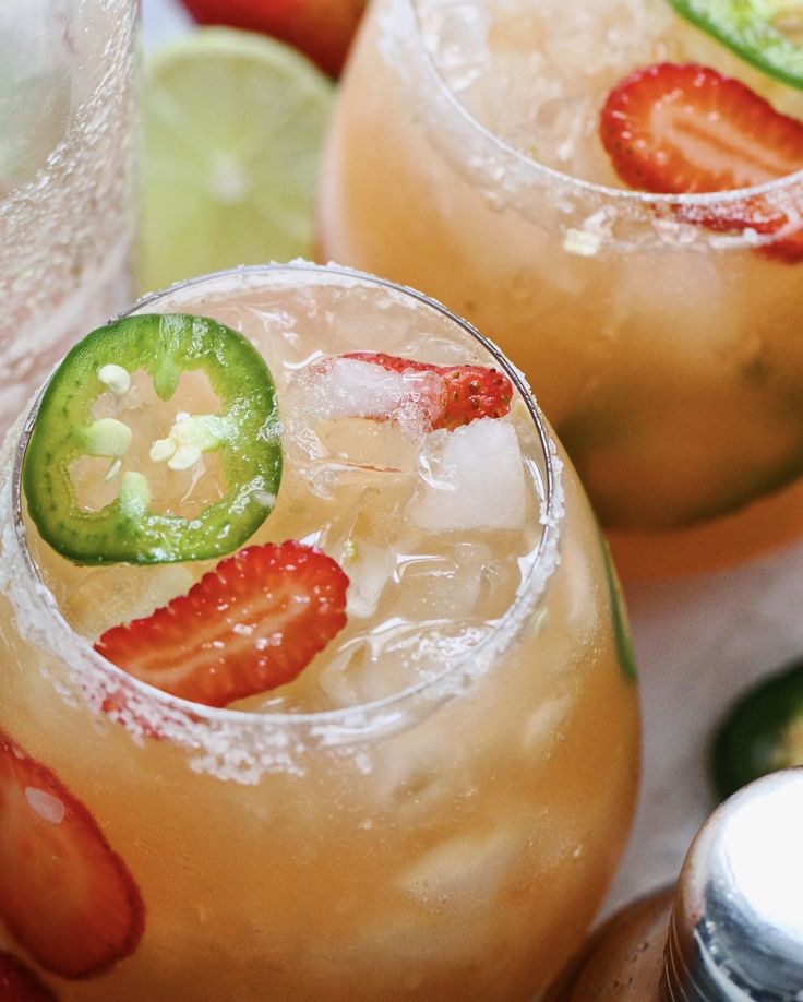 two glasses filled with fruit and ice on top of a table next to limes