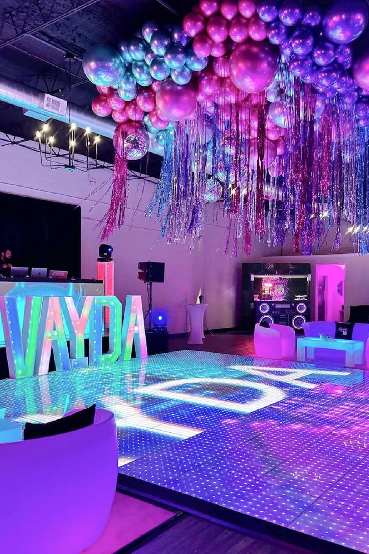 the dance floor is lit up with purple and blue lights, balloons and streamers