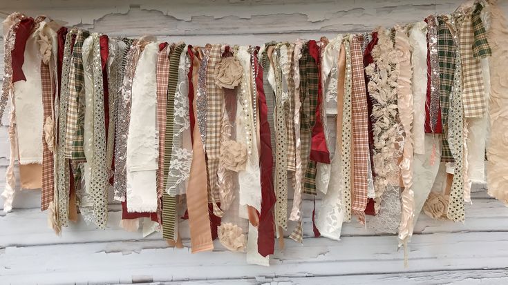 an assortment of old ribbons hanging on a white wooden wall in front of a window