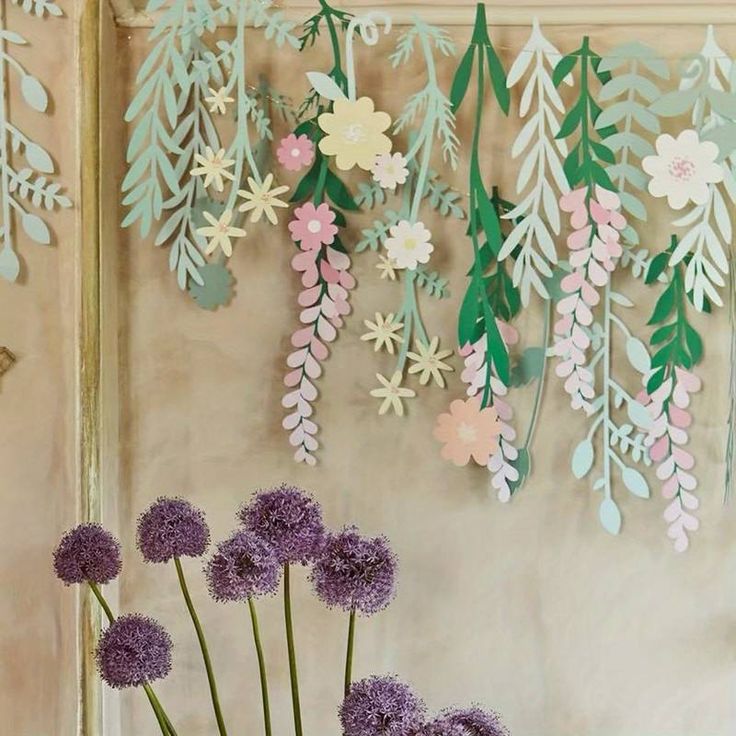 some purple flowers are in a vase on a table with green leaves and paper flowers