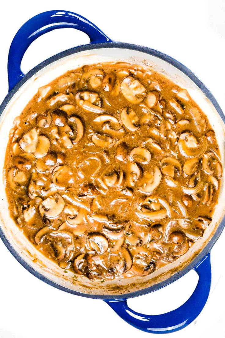 a blue pot filled with cooked mushrooms on top of a white countertop next to a red spatula