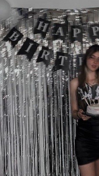 a woman holding a cake in front of a happy birthday sign with streamers behind her