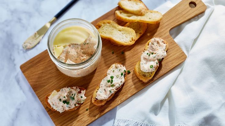 a wooden cutting board topped with slices of bread next to a jar of spread and butter