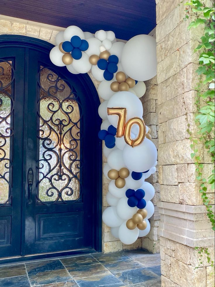 balloons are attached to the front door of a house that is decorated with gold and white balloons