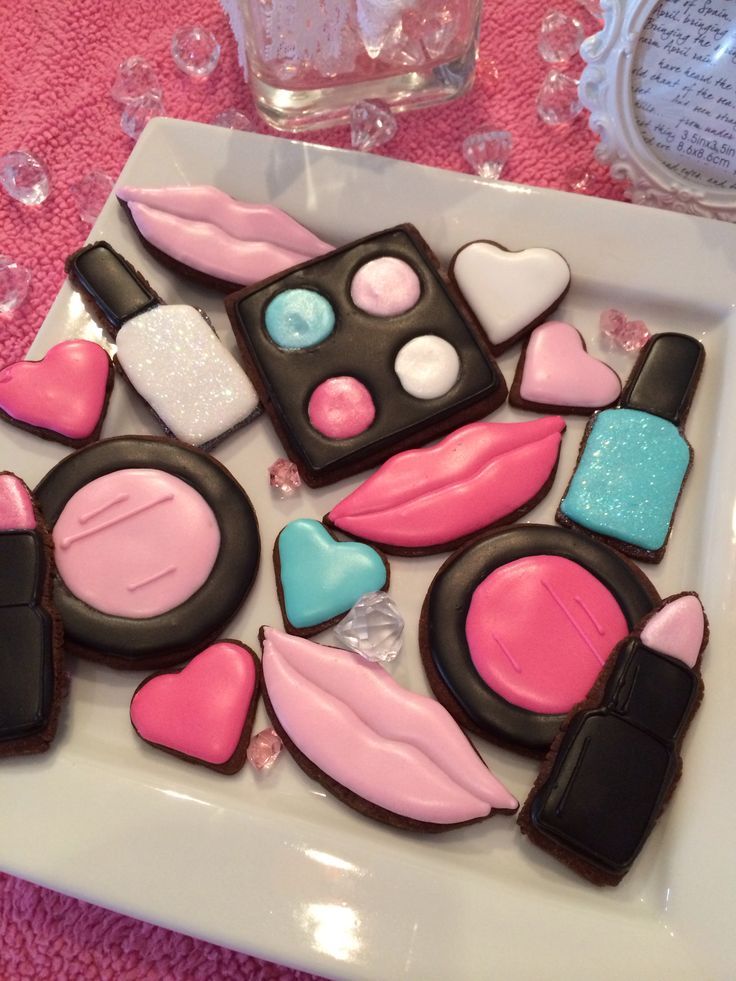 decorated cookies are arranged on a plate with pink, blue and black icing in the shape of makeup