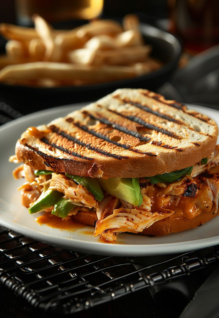 a grilled chicken sandwich on a plate with french fries in the backgroud