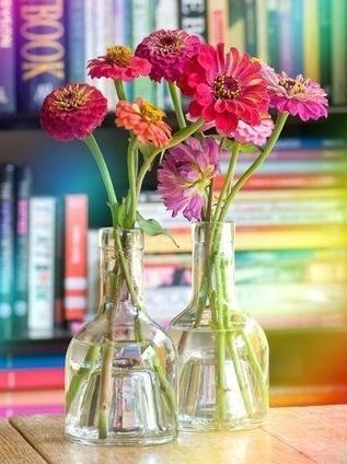 three vases filled with colorful flowers on top of a wooden table in front of bookshelves