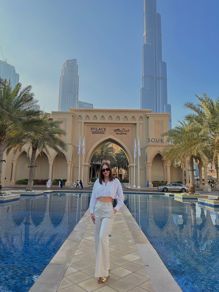 a woman standing in front of a swimming pool with the burj building in the background