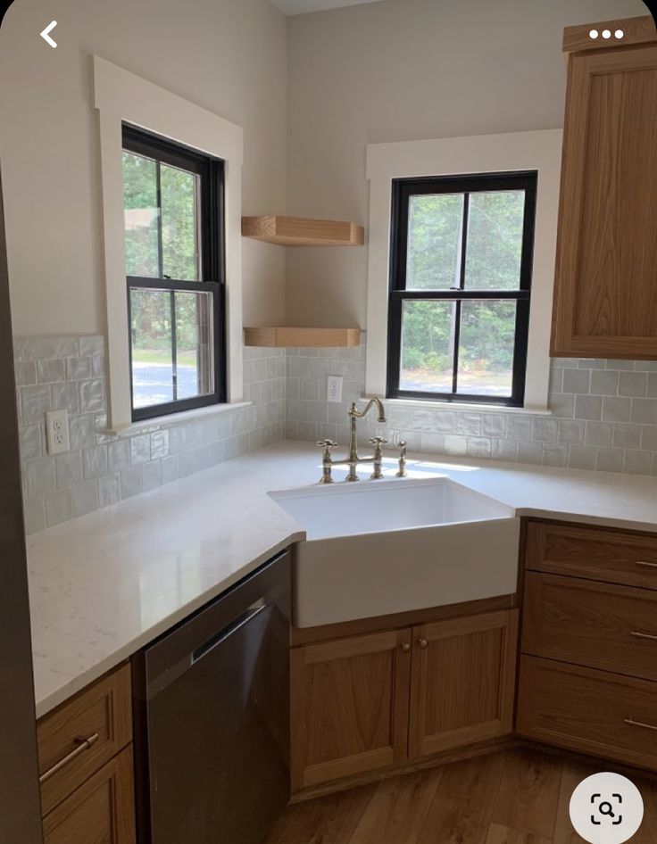 an empty kitchen with wooden cabinets and white counter tops is seen in this image, there are two windows above the sink