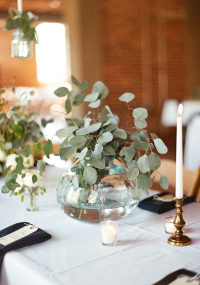 the table is set with white linens and greenery in glass vases on each side