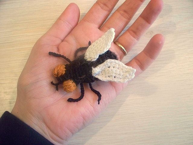 a hand holding a tiny crocheted insect on it's palm