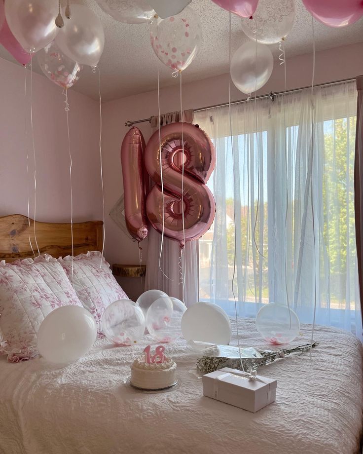 balloons floating from the ceiling above a bed with pink and white sheets on it, in front of a window