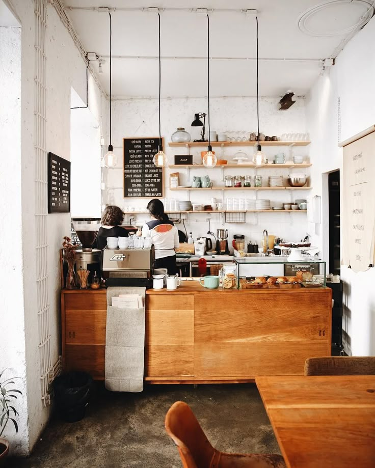 two people working behind the counter in a coffee shop with shelves on the wall above them