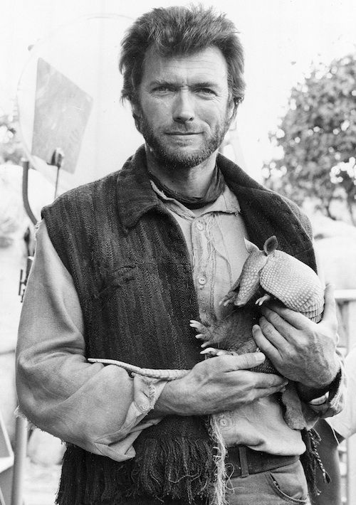 black and white photograph of a man holding a baby animal in his hands, with another person standing behind him