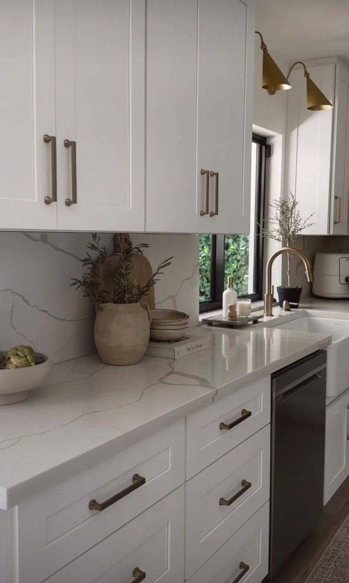 a white kitchen with marble counter tops and stainless steel dishwasher in the center