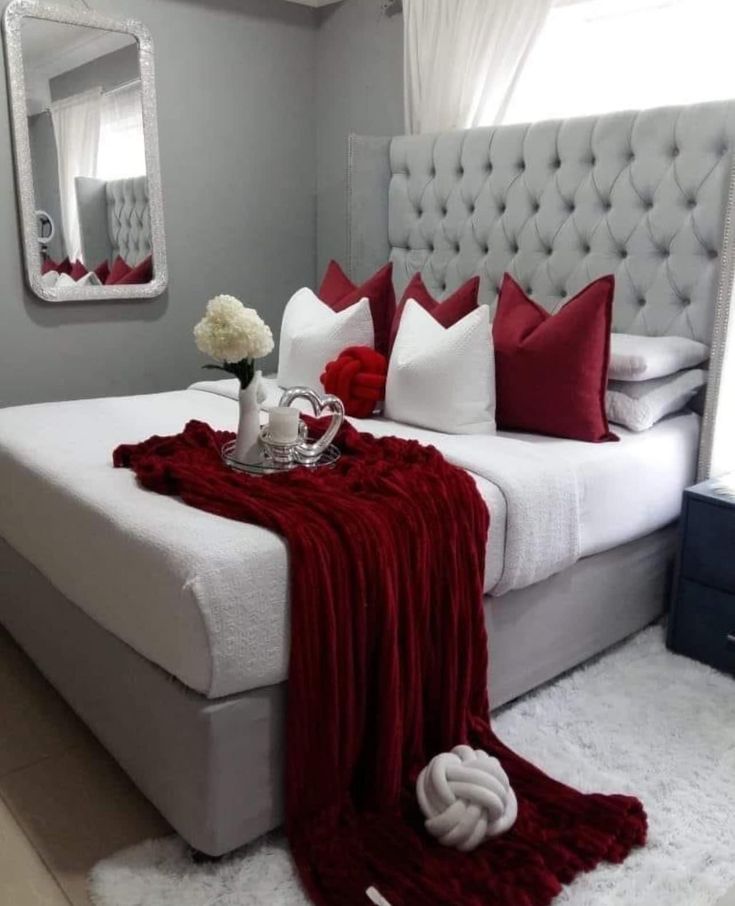 a bed with red and white pillows on top of it next to a table with flowers