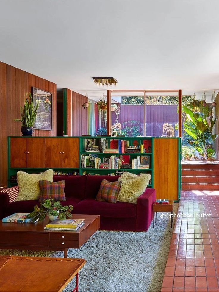 a living room filled with furniture and bookshelves next to a window covered in plants