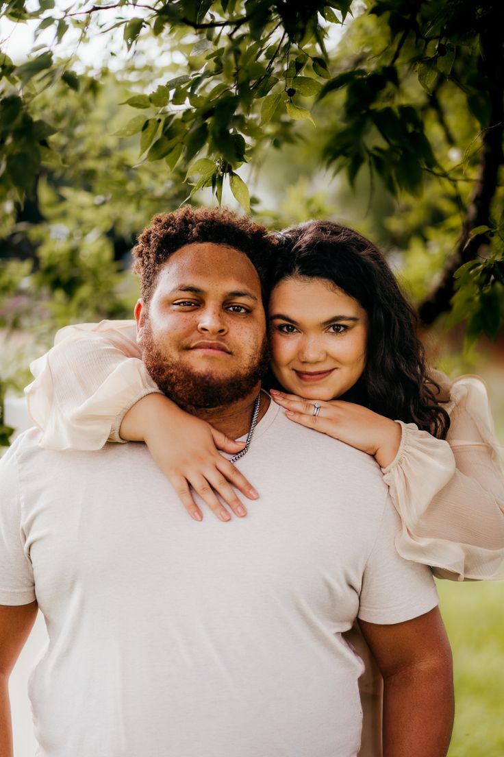 a man and woman are standing under a tree, one is holding his arm around the other's shoulder