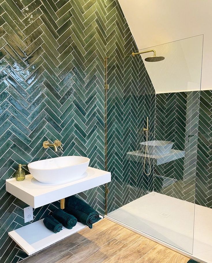 a bathroom with green tiles on the wall and wooden flooring, along with a white sink