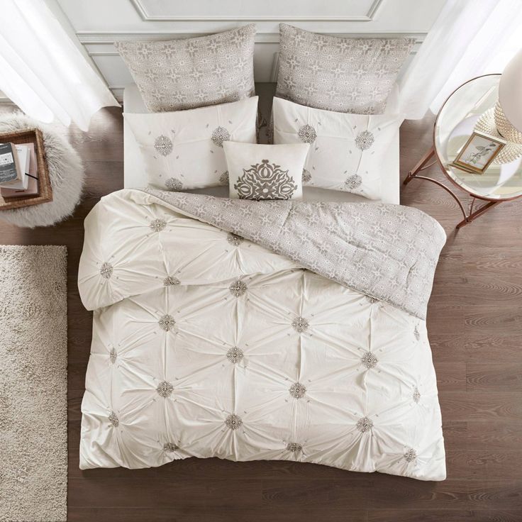 a bed with white comforter and pillows on top of it next to a mirror