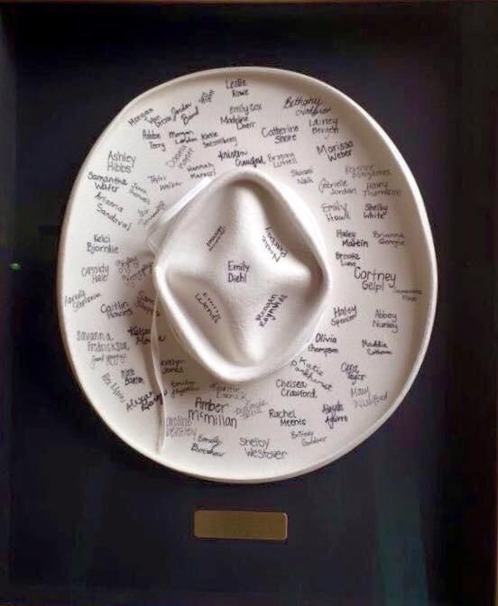 a white hat with writing on it is in a shadow box that holds a plate