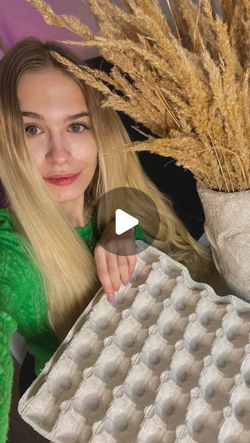 a woman holding an egg carton in front of her face and wheat stalks behind her