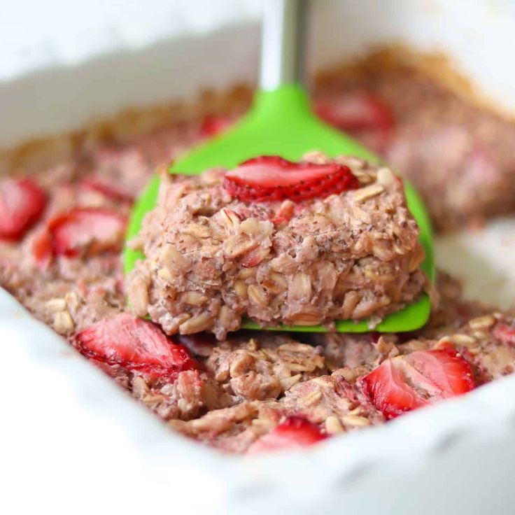 a green ladle scooping out some oatmeal with strawberries on top