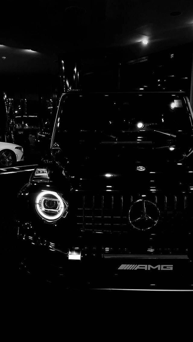 the front end of a black mercedes car in a showroom with its lights on