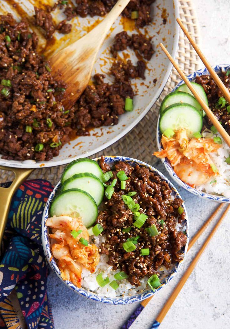 two bowls filled with rice, meat and cucumber on top of a table