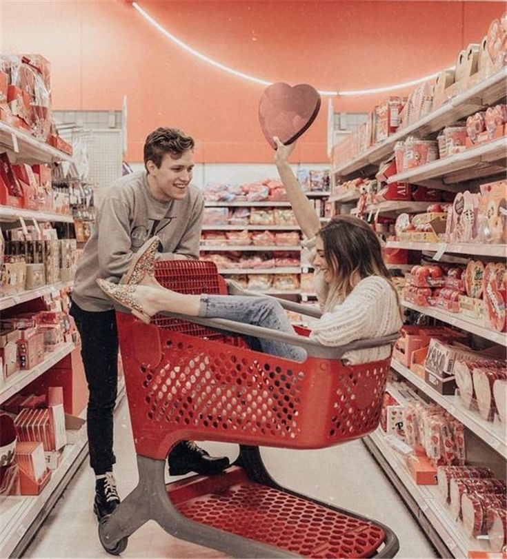 a man and woman pushing a shopping cart through a store aisle