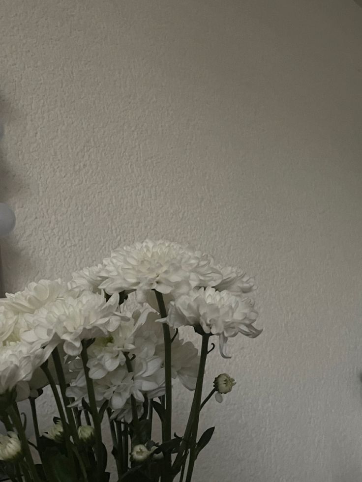 a vase with white flowers in it sitting on a table next to a wall clock