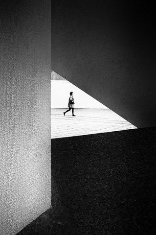 black and white photograph of a person walking in an open space with shadows on the wall