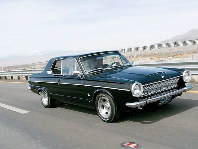 an old black car driving down the road