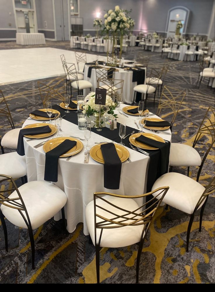 the tables are set up with black and white linens, gold chargers, and centerpieces