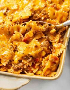 a casserole dish filled with ground beef, cheese and pasta is being spooned into the casserole