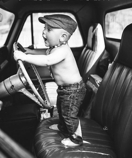 a young boy sitting in the driver's seat of a car holding a steering wheel