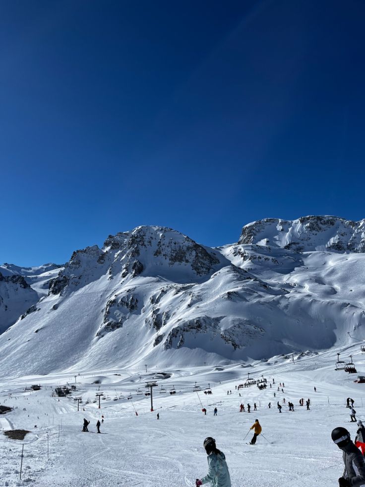 a group of people riding skis on top of a snow covered slope with mountains in the background